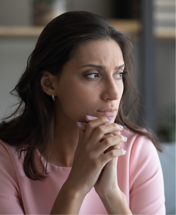 A woman who appears to have anxiety or depression clasps her hands together, holding them to her lips with a frown