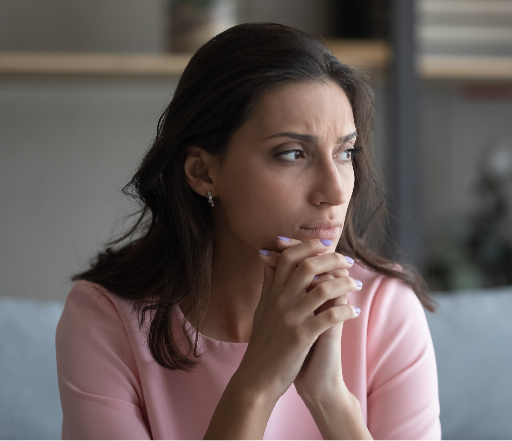 A woman who appears to have anxiety or depression clasps her hands together, holding them to her lips with a frown